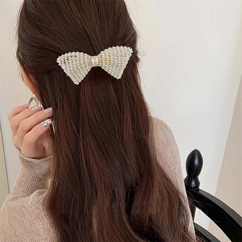 Gold-tone A549 pearl-look and rhinestone bow barrette in a half-up hairstyle. Supplier styling example.