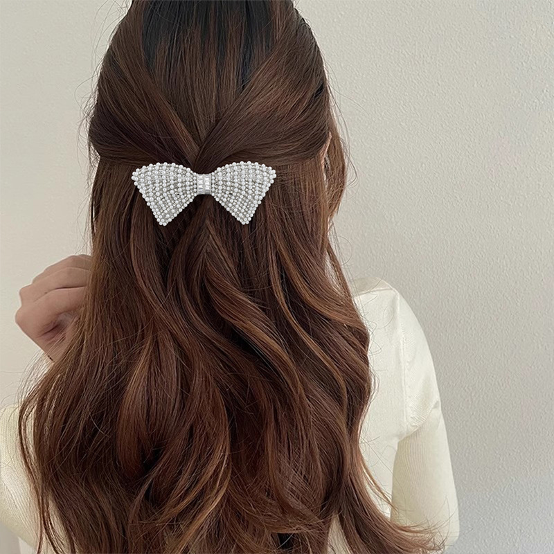 Silver-tone A549 pearl-look and rhinestone bow barrette in a half-up hairstyle. Supplier styling example.