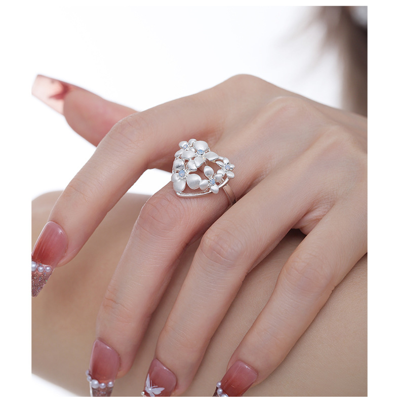 Silver-tone openwork heart and flower ring with pale blue centers worn on a hand