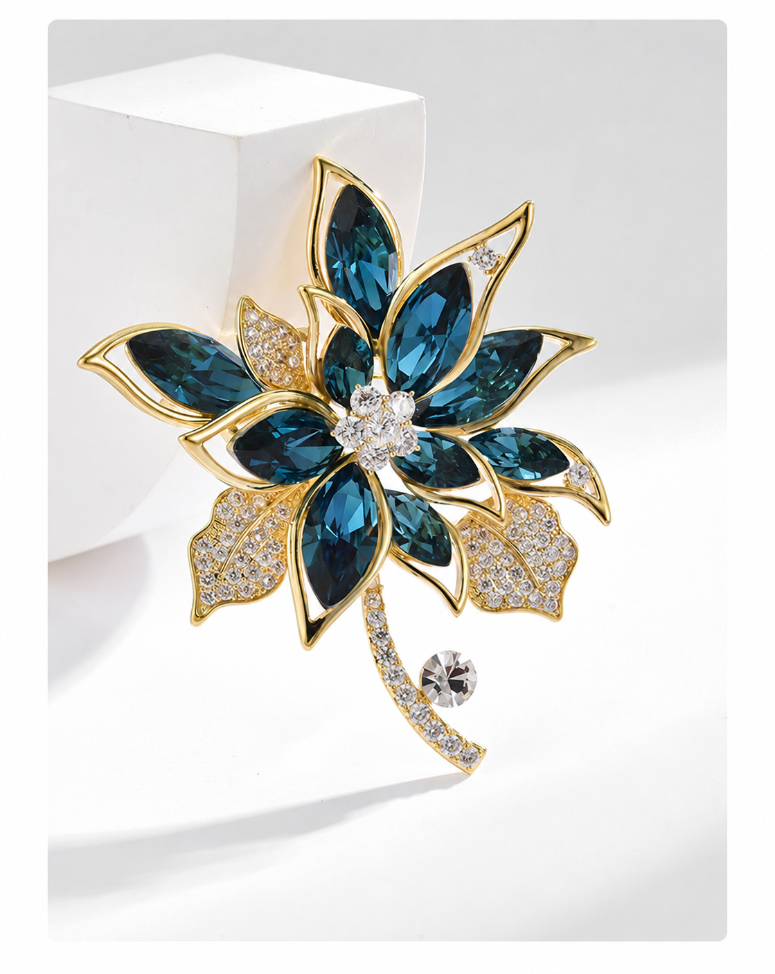 Gold-tone flower brooch with deep blue faceted petals, clear stone leaves and a curved stem