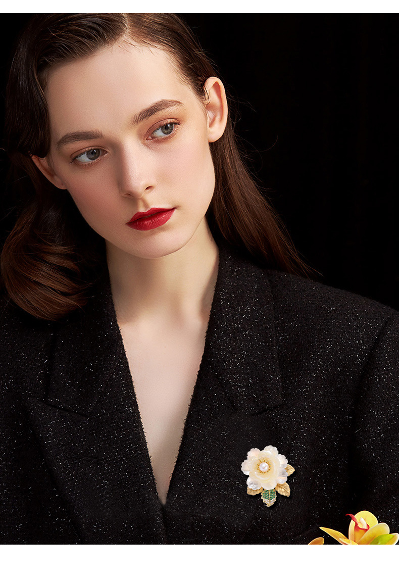 Styling illustration of an ivory shell flower brooch with a pearl center on a black jacket