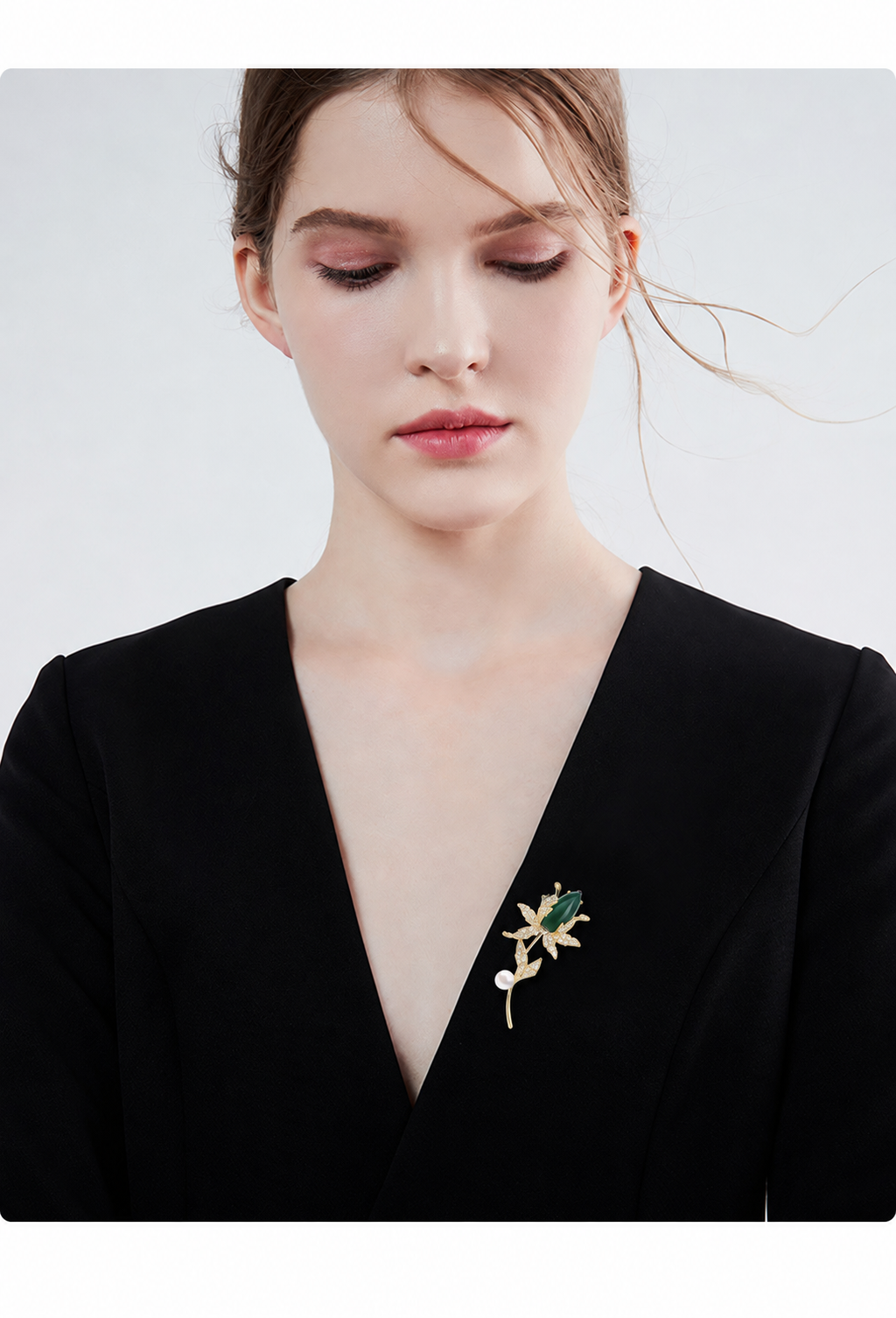 Green and gold-tone magnolia brooch with a freshwater pearl styled on a black garment
