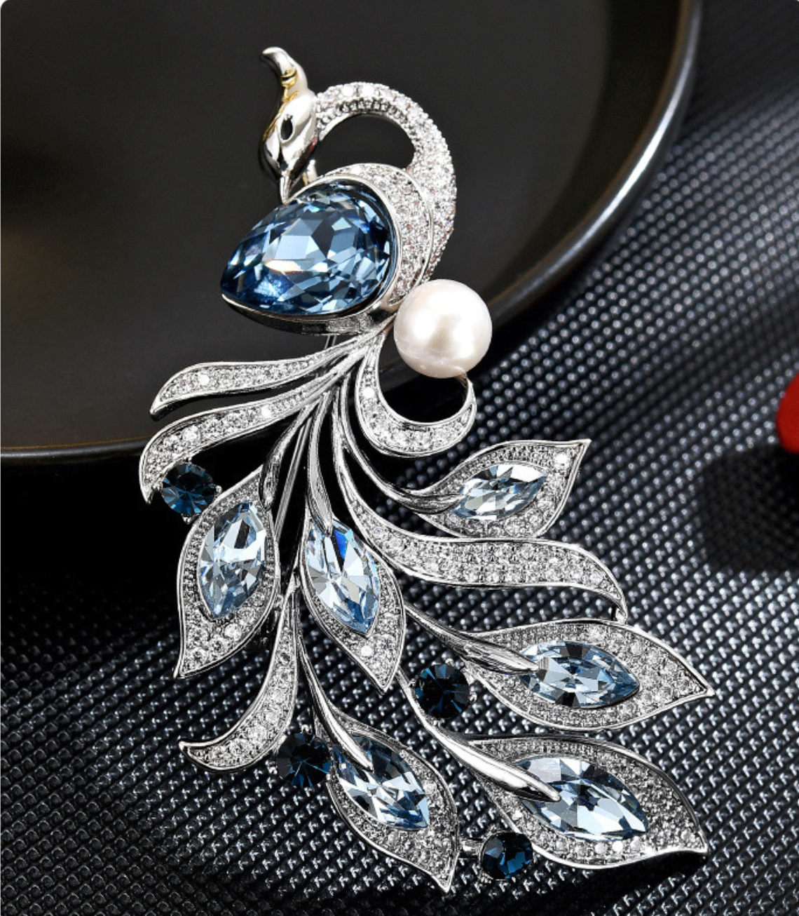 Close-up of the blue faceted stones and pearl-look accent on the silver-tone phoenix brooch