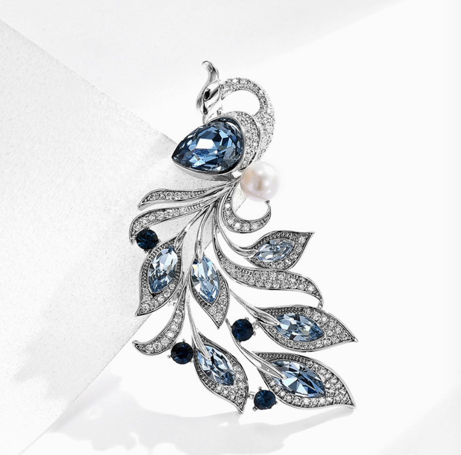Silver-tone phoenix brooch with a blue teardrop stone, flowing blue-stone feathers and a white pearl-look accent