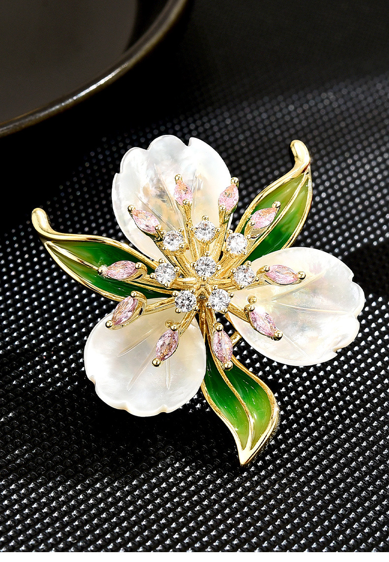 Gold-tone flower brooch with three pearlescent petals, green leaves, and pink and clear decorative stones