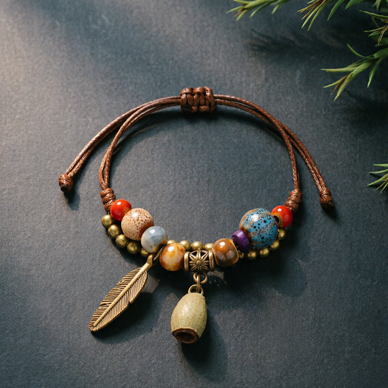 Bell Pod charm bracelet with ceramic beads, brown adjustable cord and bronze-tone feather detail