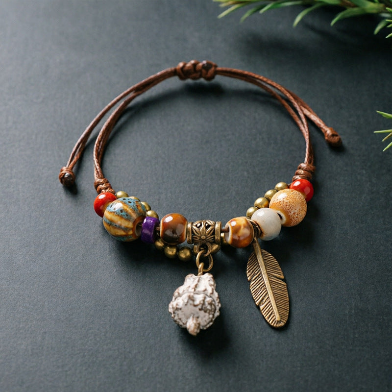 Textured Eucalyptus Pod charm bracelet with ceramic beads, brown adjustable cord and bronze-tone feather detail
