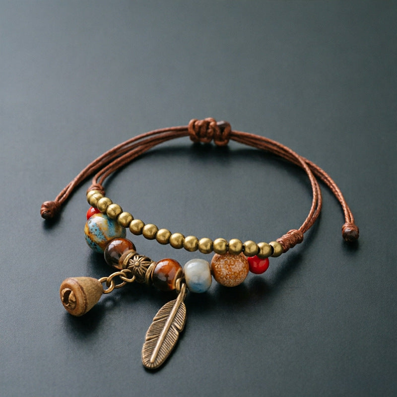 Small Bell Pod charm bracelet with ceramic beads, brown adjustable cord and bronze-tone feather detail