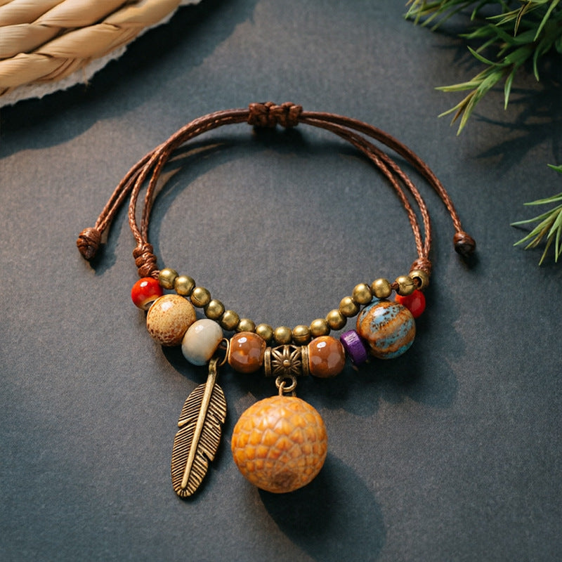 Lychee Charm charm bracelet with ceramic beads, brown adjustable cord and bronze-tone feather detail