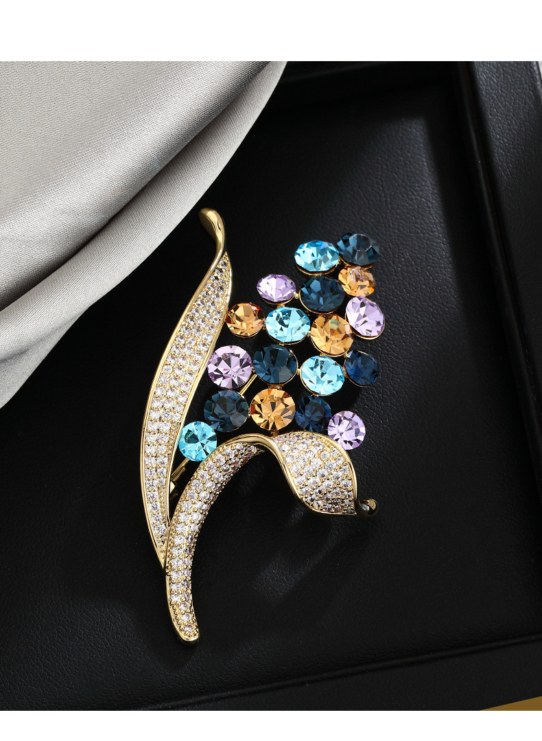 Multicolor floral brooch with gold-tone leaves on a black background