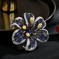Blue lily brooch with curved stone-set petals, clear sparkling edges and raised gold-tone stamens on a dark background
