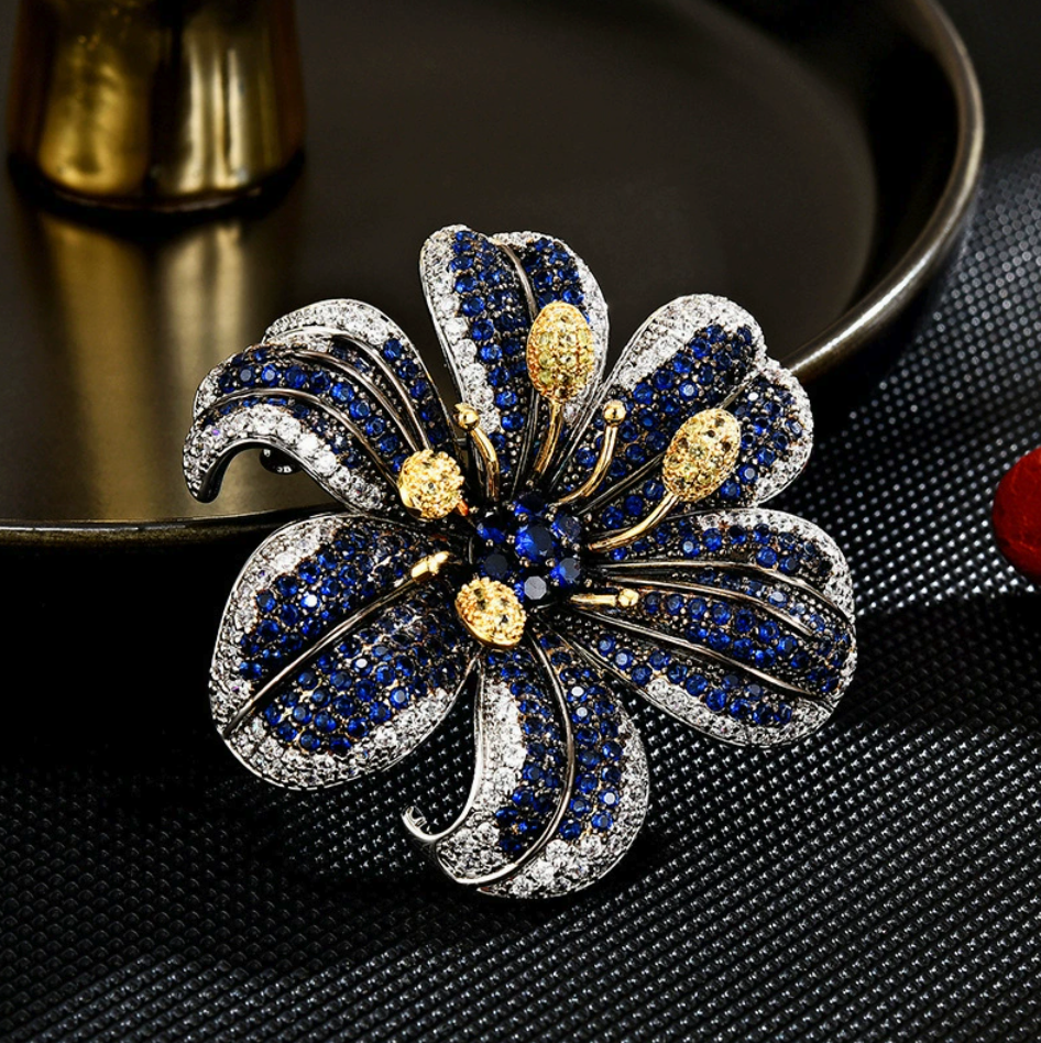 Blue lily brooch with curved stone-set petals, clear sparkling edges and raised gold-tone stamens on a dark background