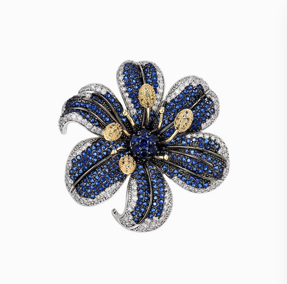Blue lily flower brooch with sparkling blue and clear stones and gold-tone stamens on a white background