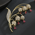 Pink lily-of-the-valley brooch with a gold-tone frame, clear decorative stones and six pink teardrop accents