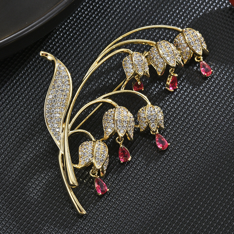 Pink lily-of-the-valley brooch with a gold-tone frame, clear decorative stones and six pink teardrop accents