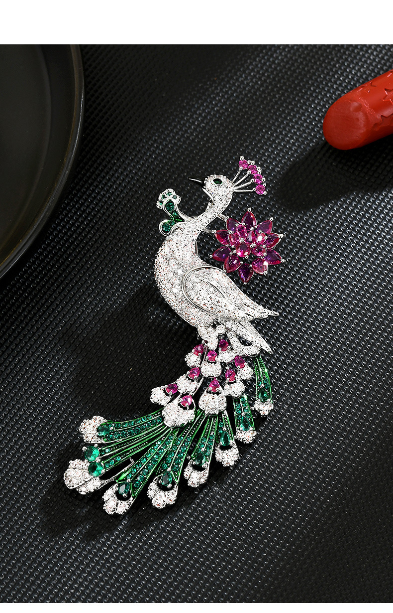 Silver-tone peacock brooch with a pink flower, sparkling clear body and long green feather tail