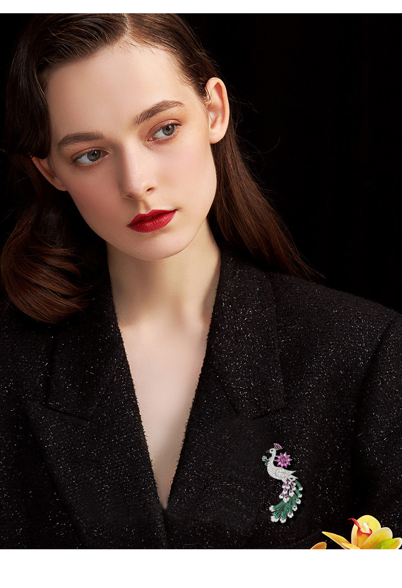 Pink and green peacock brooch worn on the lapel of a black jacket