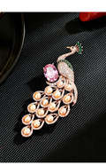 Rose-gold-tone peacock brooch with pink and green stone accents and freshwater pearls on a black textured surface