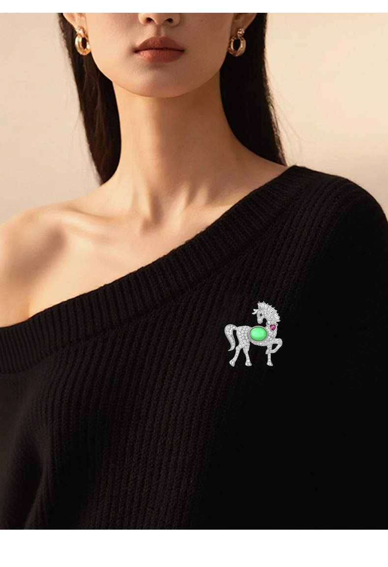 Silver-tone horse brooch with green and pink accents styled on a black knit top