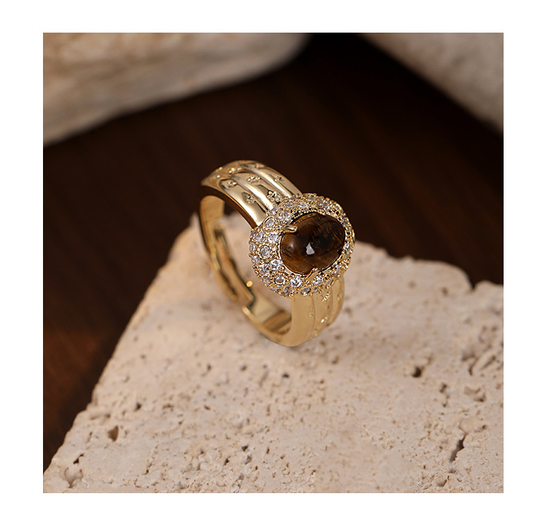 Angled view of the oval brown centerpiece, clear stone halo and star-patterned gold-tone band
