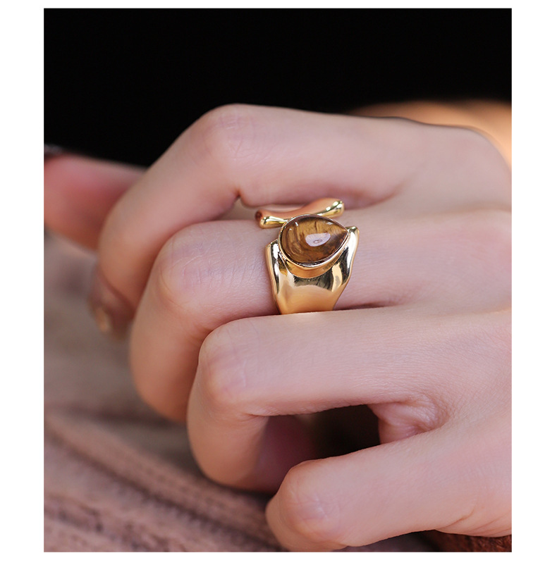 Brown teardrop tiger's eye ring with a polished gold-tone open band worn on a hand
