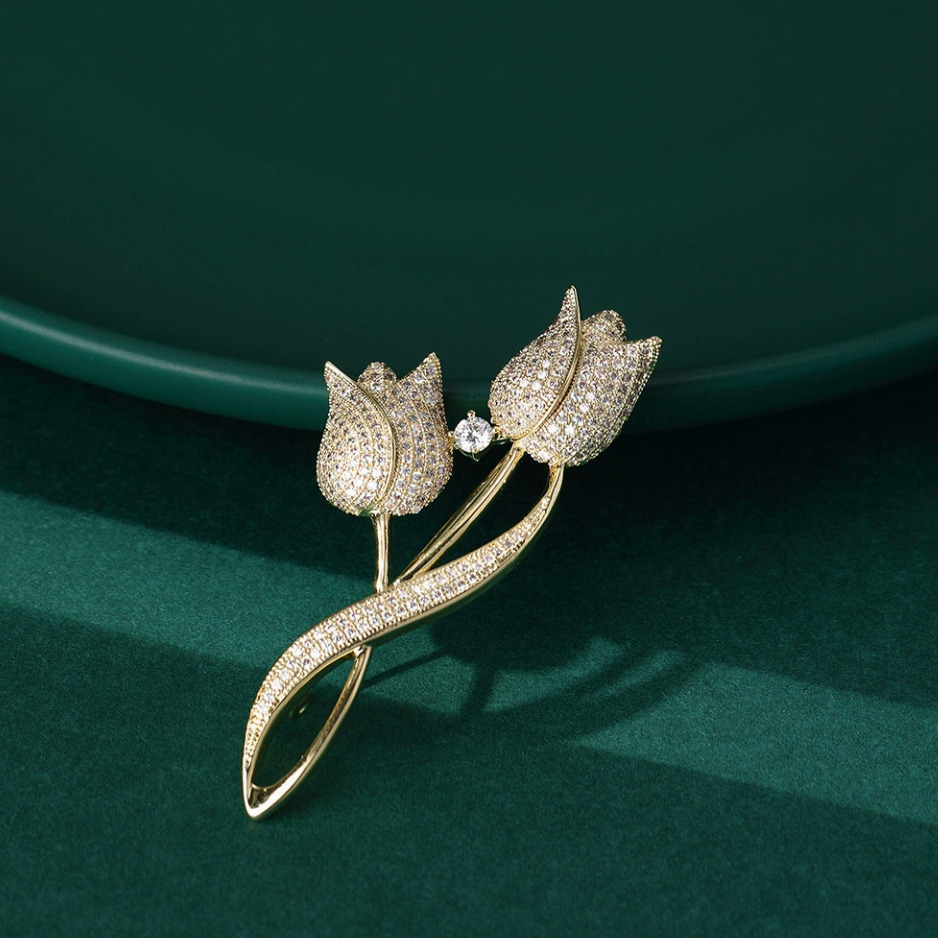 Gold-tone twin tulip brooch showing the stone-set blooms and curved leaf against a deep green background