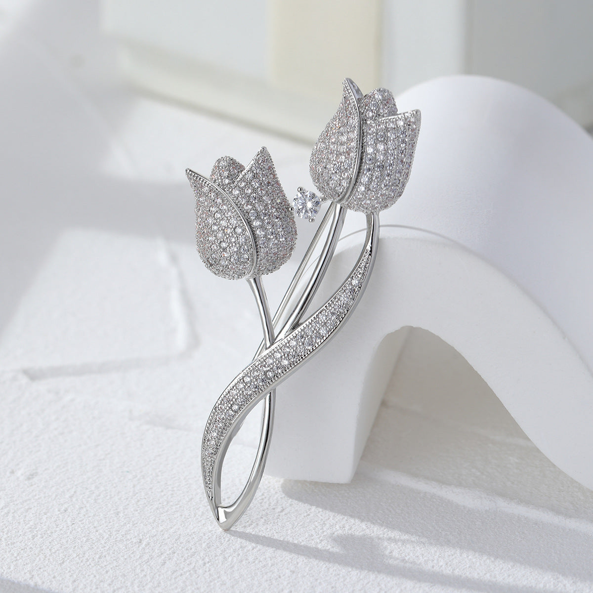 Silver-tone twin tulip brooch with sparkling clear stones and a flowing open-loop stem on a light background
